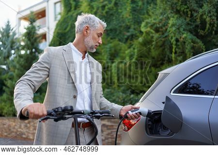 Close Up Of Businessman In Suit On Way To Work Standing At Eletric Scooter And Charging His Electric