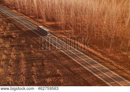 Semitrailer Eighteen-wheeler Truck On The Road Through Deciduous Forest Landscape In Autumn Sunset, 