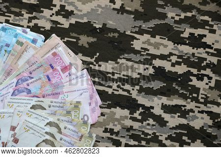 Ukrainian Hryvnya Bills On Fabric With Texture Of Ukrainian Military Pixeled Camouflage. Cloth With 