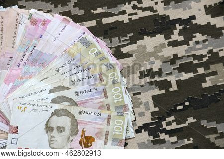 Ukrainian Hryvnya Bills On Fabric With Texture Of Ukrainian Military Pixeled Camouflage. Cloth With 