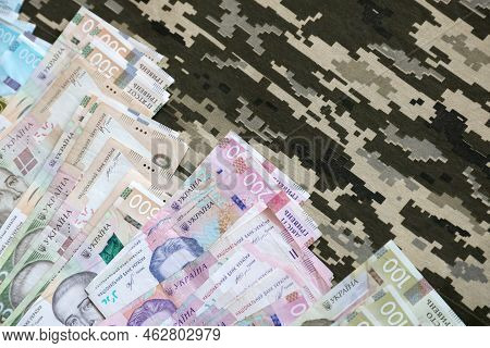 Ukrainian Hryvnya Bills On Fabric With Texture Of Ukrainian Military Pixeled Camouflage. Cloth With 