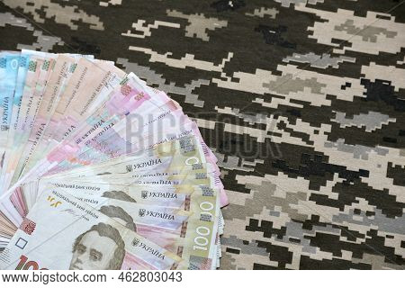 Ukrainian Hryvnya Bills On Fabric With Texture Of Ukrainian Military Pixeled Camouflage. Cloth With 
