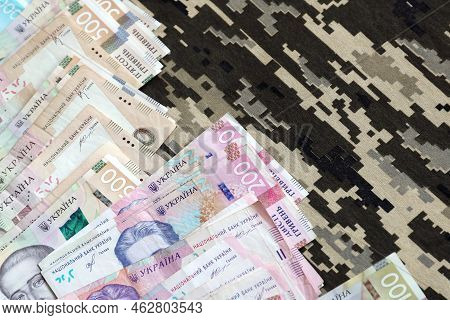 Ukrainian Hryvnya Bills On Fabric With Texture Of Ukrainian Military Pixeled Camouflage. Cloth With 