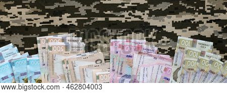 Ukrainian Hryvnya Bills On Fabric With Texture Of Ukrainian Military Pixeled Camouflage. Cloth With 