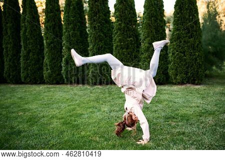 Little Beautiful Girl Somersaults On Green Field At Sunny Day.