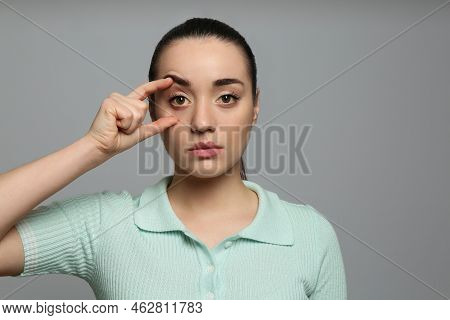 Woman Checking Her Health Condition On Grey Background. Yellow Eyes As Symptom Of Problems With Live