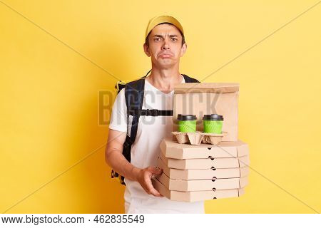 Horizontal Shot Of Sad Delivery Man Wearing White T Shirt Holding Food Order Pizza Boxes And Coffee,