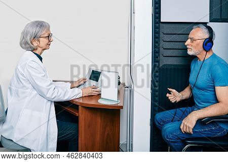 Audiological Exam. Audiologist Doing Hearing Check-up To Senior Man In Soundproof Audiometric Booth.
