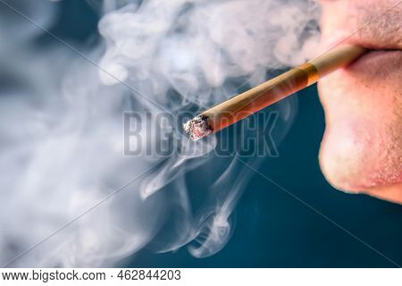 A Man Holds A Cigarette In His Mouth. He Blew Out Puffs Of Smoke.