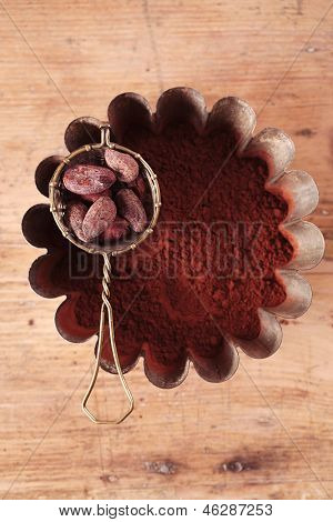granos de cacao en tamiz con cacao en polvo en hojalatería sobre fondo de madera