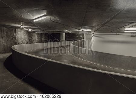 Way Down To Underground Car Parking. Perspective View Of Curving Shaped Ramp Of The Basement Made Of