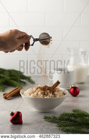 Sprinkle Cinnamon Over Scandinavian Rice Porridge In A Bowl Surrounded By Christmas Balls. Breakfast