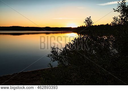 Sunset With Reflection On A Swedish Lake In Smalland With Bushes In The Foreground On The Shore. Rom