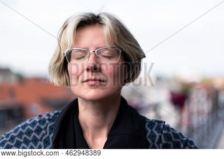 Portrait Of An Attractive Thirty Year Old Woman Posing On A Terrace, Eyes Closed, Brussels, Belgium