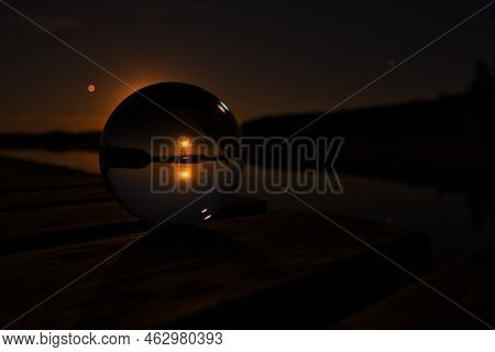 Glass Ball On A Wooden Pier At A Swedish Lake At Night. Stars And Moon In The Background. Nature Sho