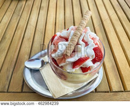 A Strawberry Sundae With Whipped Cream And Waffle Is On A Table.
