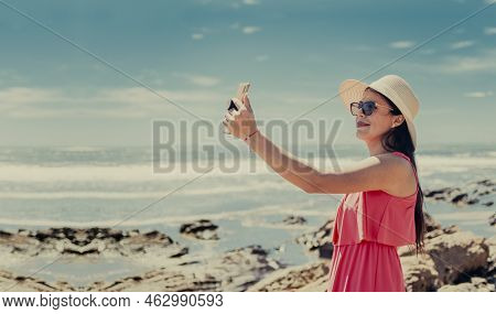 Young Woman On Vacation Taking Photos On The Beach, Smiling Girl In Hat Taking Photos On The Beach.
