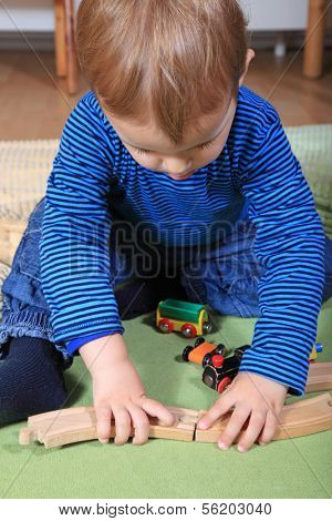 Cute caucasian toddler playing with toy train in kindergarten.