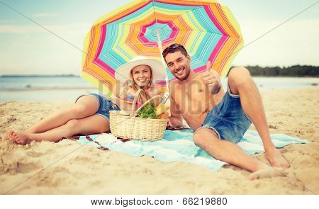 summer, holidays, vacation and happy people concept - smiling couple lying on the beach under colorful umbrella and showing thumbs up