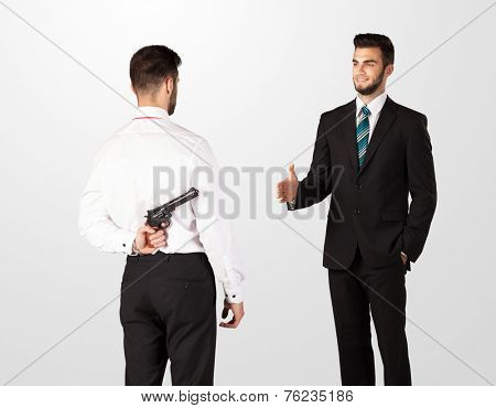 Two opposing businessman shake hands, one of them hiding a weapon behind his back