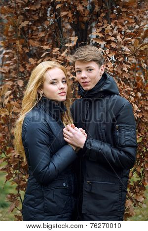 Happy teen couple in love holding each other on the background of autumn leaves