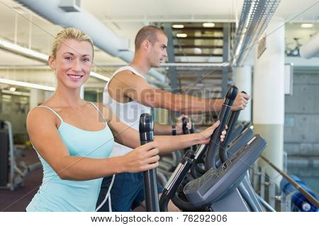 Side view of a fit young couple working on x-trainers at the gym