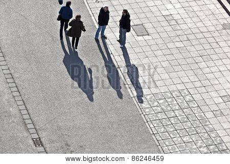 People Walking At The Street With Long Shadows