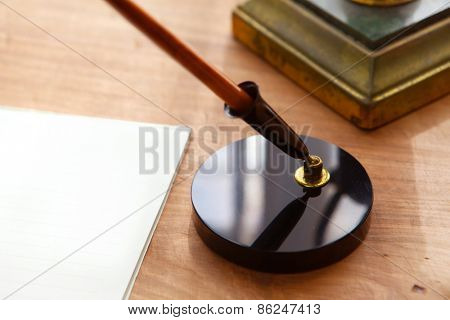 Retro style pen, pen stand and paper or memo on wooden desk.  Focus is on pen base. Shallow depth of field