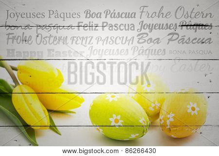 Happy easter in different languages against three easter eggs with yellow tulips
