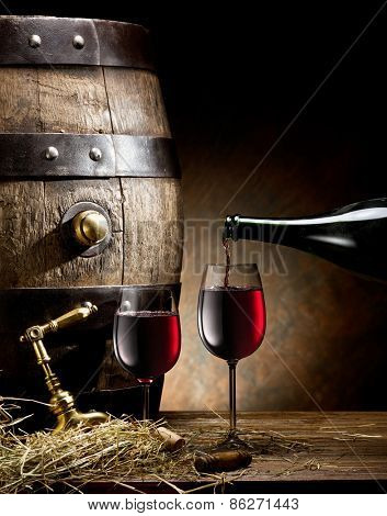 Still-life with glass of wine, bottle and barrel on the table in the cellar.