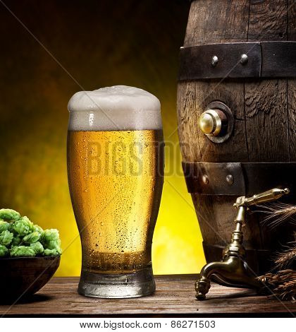 Still life: old wooden pin of beer, glass of beer and wheat on the table in the cellar.