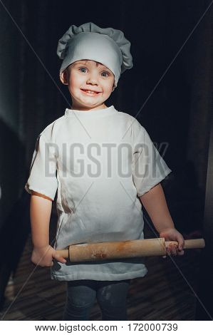 Baby cook with a rolling pin on a black background