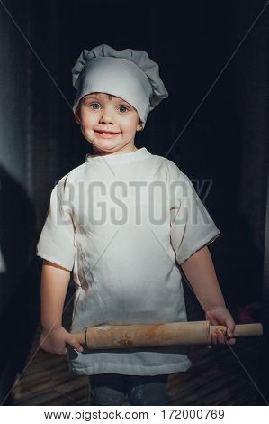 Baby cook with a rolling pin on a black background
