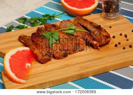 Grilled pork ribs on a cutting board with black pepper, coriander and sliced grapefruit.