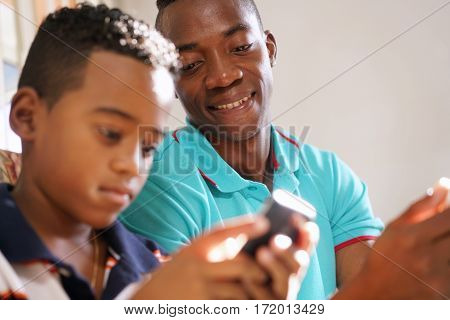 Happy black family at home. African american father and child playing game with cell phone. Hispanic dad and son having fun with smartphone.