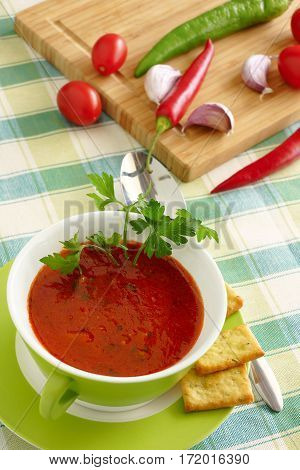 Tomato soup in a green bowl.Tomatoes, pepper and garlic on a cutting board