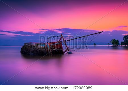 An old shipwreck or abandoned shipwreck Boat capsized on beach in beautiful sunset background Thailand.