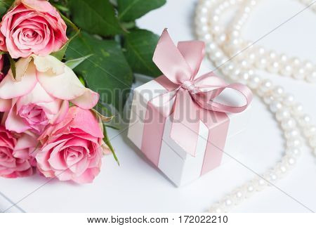 Gift box with pink ribbon and rose flowers on white table