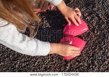 Little Girl Playing With A Red Plastic Heart. She Holds It In Her Hands