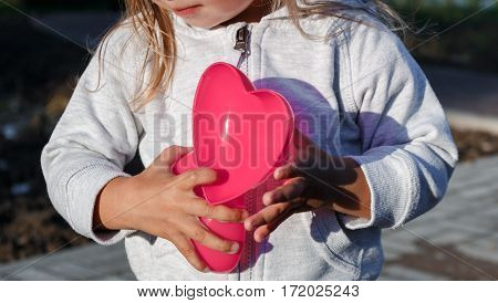 Little Girl Playing With A Red Plastic Heart. She Holds It In Her Hands