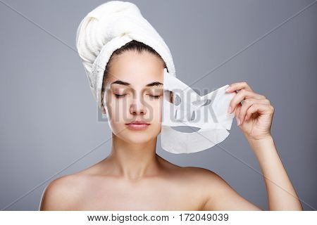 Girl with almost rended white mask. Model pulling away mask from her face. Closed eyes. Head and shoulders, studio, indoors