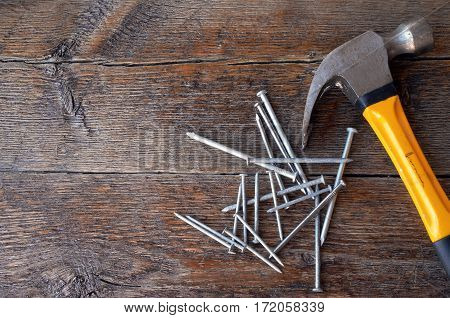 A top view image of an old used yellow hammer and a pile of nails on a wooden workbench.