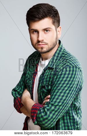 Man in green checked T-shirt half turned aside, looking at camera. Young man, casual style. Half turn, waist up. Hands crossed. Indoors, studio