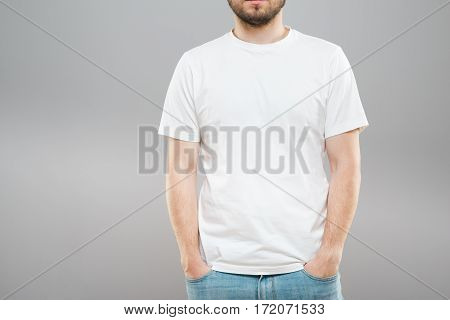 Man with beard in white T-shirt and jeans. Mockup. Hands in pockets. Portrait without head. Indoors, studio