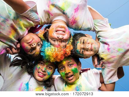 five Indian kids making circle on holi, Asian small kids or siblings or friends with heads together in round, with faces coloured with gulal