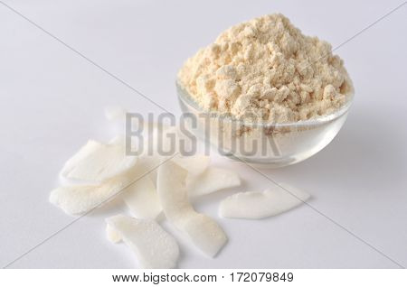 Coconut flour and flakes on white background. Cream powder in a glass bowl. Isolated on white. Alternative gluten-free flour for baking and cooking