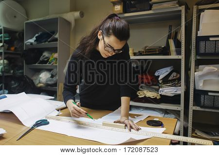 female fashion desighner draws dress template on panel table in workshop interior