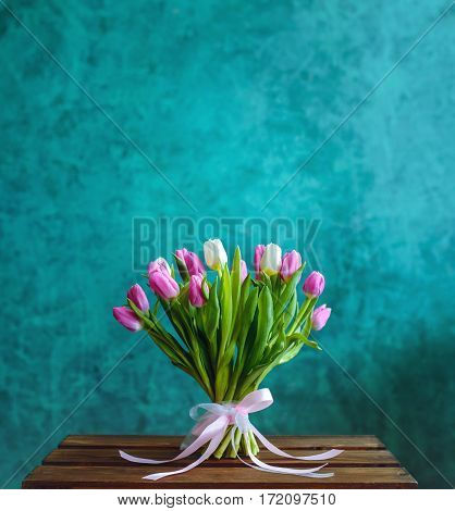 Bouquet of pink and white tulips with pink ribbon on the green painted wall background and empty space for text.
