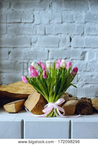 Bouquet of tulips with pink ribbon on the gray brick wall and firewood background