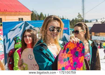 Group Of Young Happy Pretty Women On A Snowboard In Colorful Bikini With Flags.